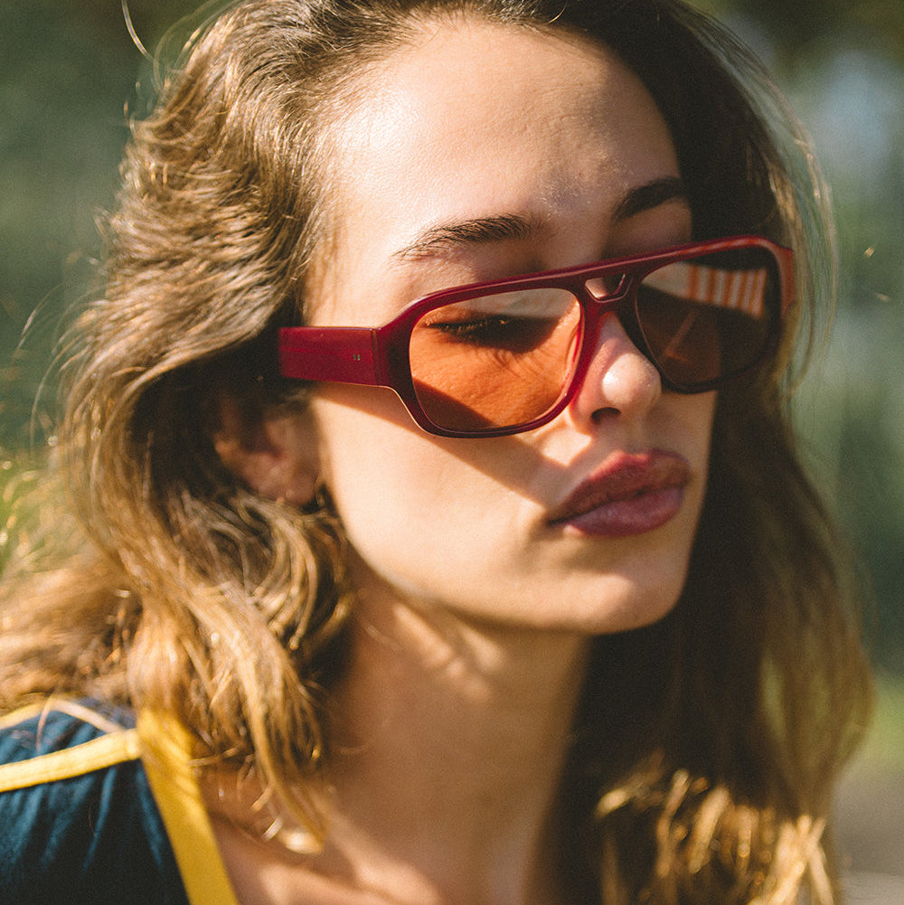 Woman wearing red aviator sunglasses with a blurred natural background
