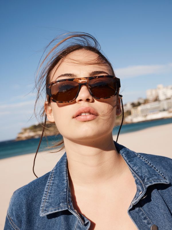 Woman wearing Sito Shades brown tort aviator sunglasses with a beach and ocean view in the background