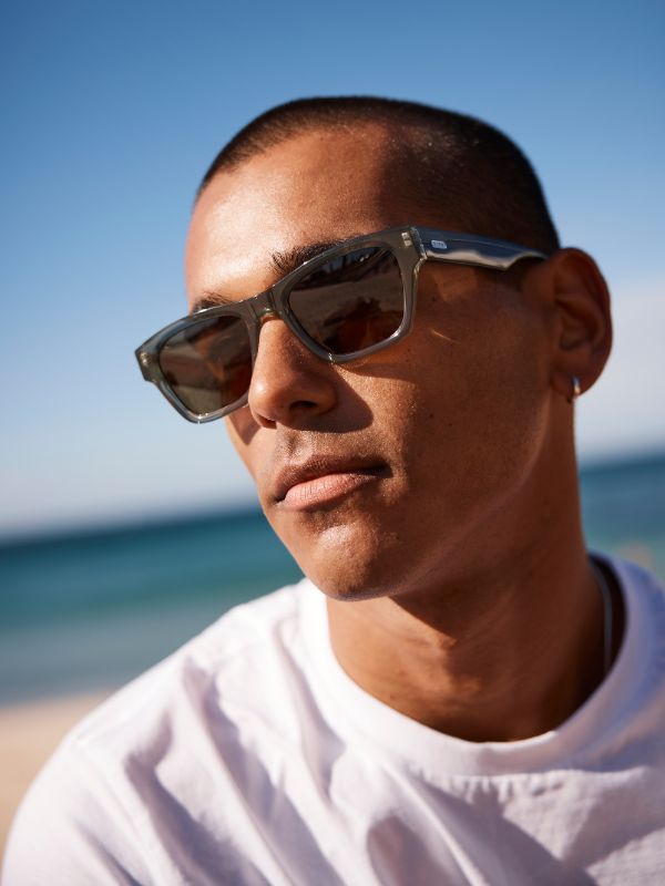 Man in white tshirt wearing green sunglasses with a beach background