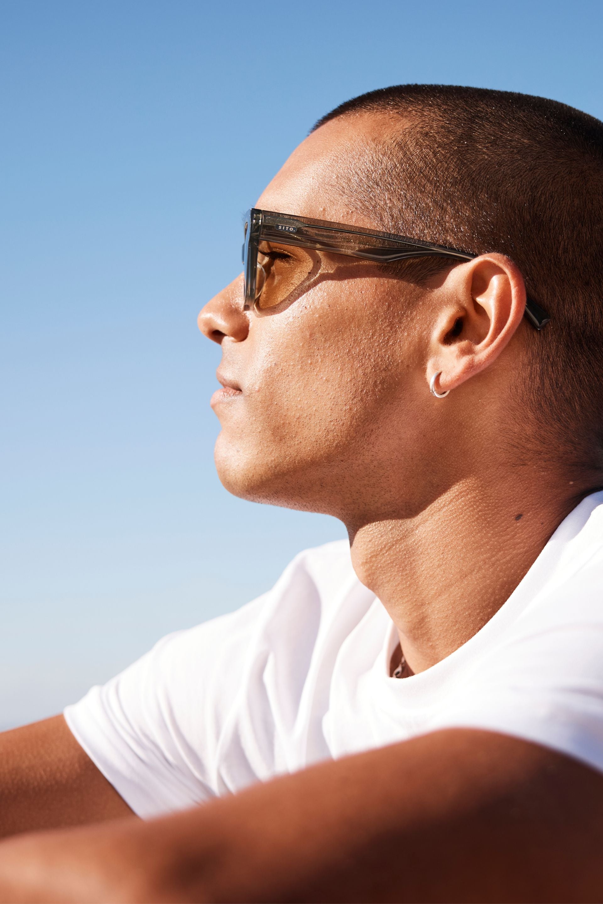 Man wearing white tshirt looking into the sunlight with green Sito Shades sunglasses
