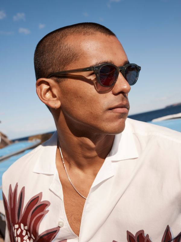 Man wearing Sito Shades Elio Nori green sunglasses and a white shirt with a floral pattern on a boat.