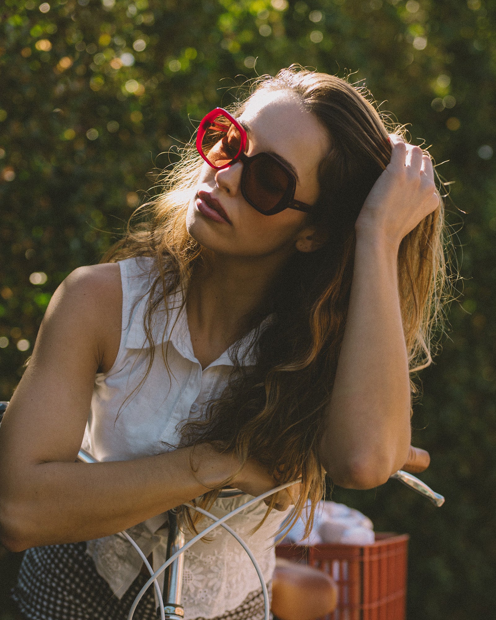 Woman wearing red oversized retro sunglasses outdoors with a blurred green background