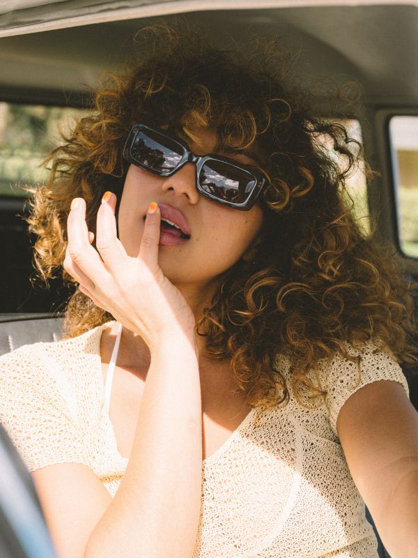 Woman with rectangle brown Sito Shades sunglasses and curly hair sitting inside a vehicle