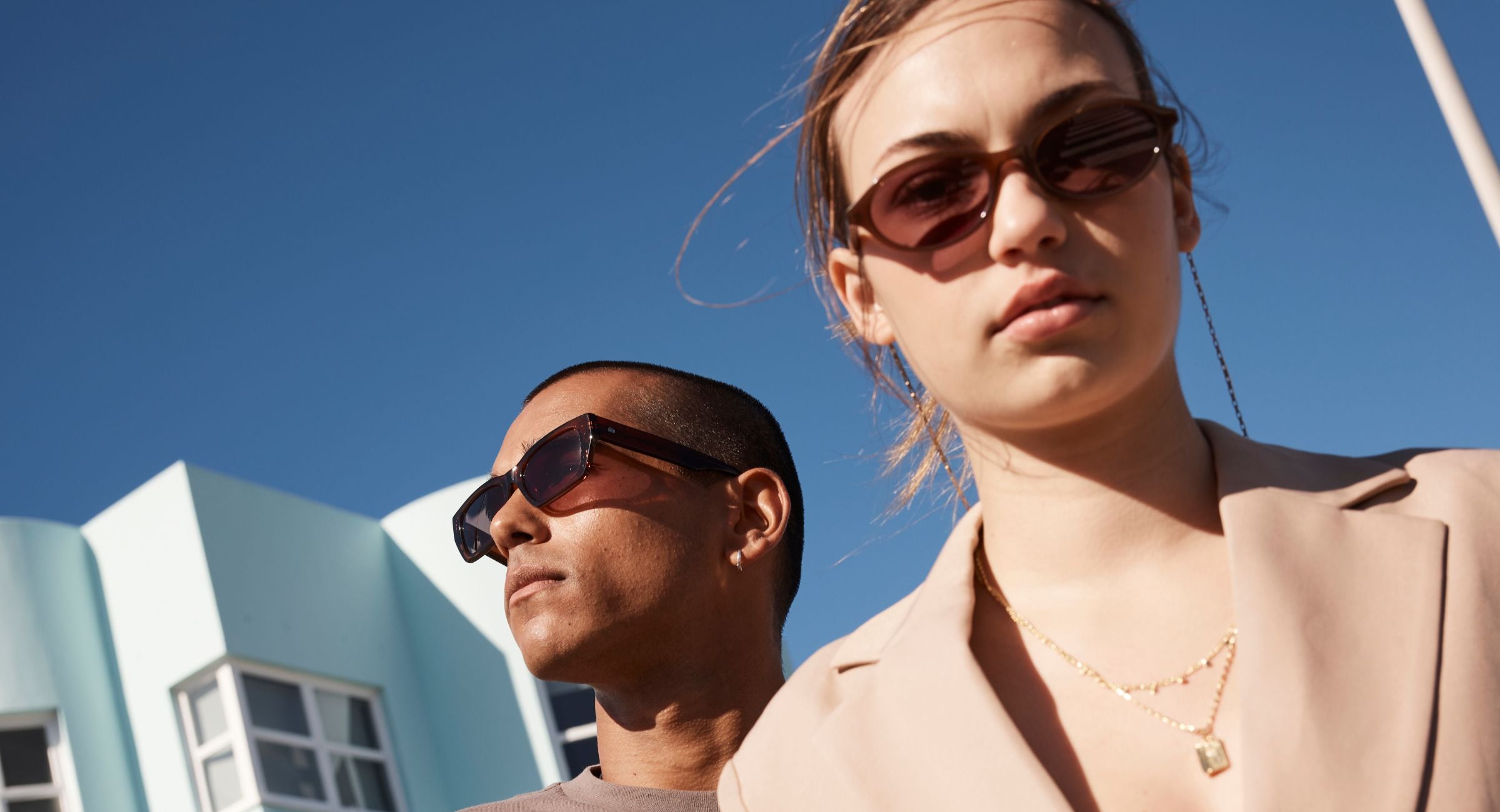 A man and women wearing Sito Shades sunglasses with a clear blue sky and building in the background.