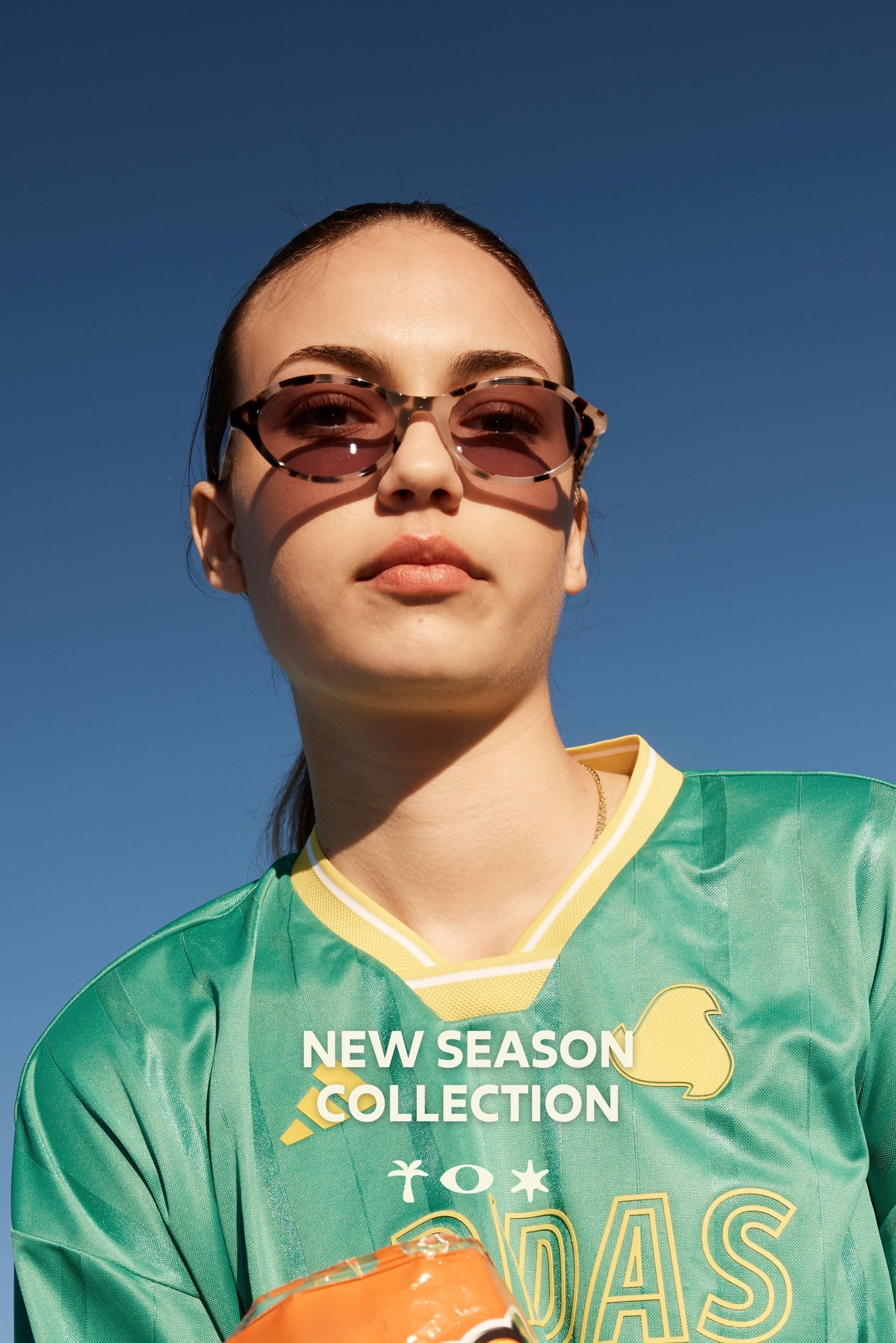 Person wearing 'New Season Collection' Sito Shades sunglasses and a green jersey against a blue sky.