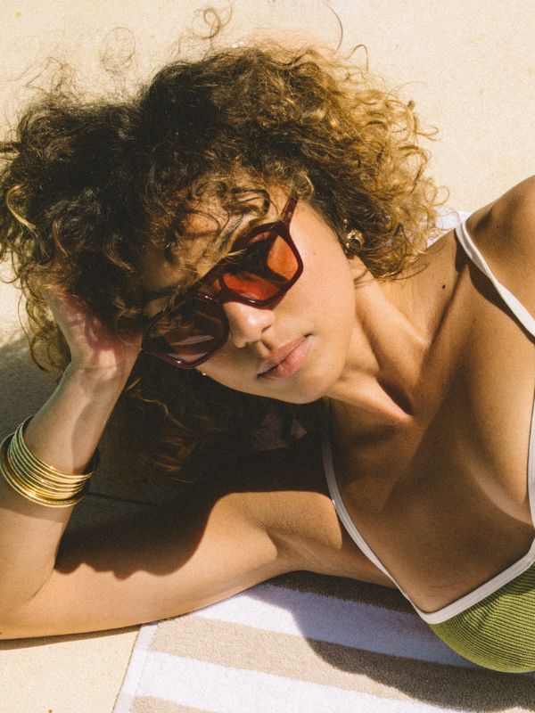 Woman laying on a towel wearing red aviator sunglasses by Sito Shades