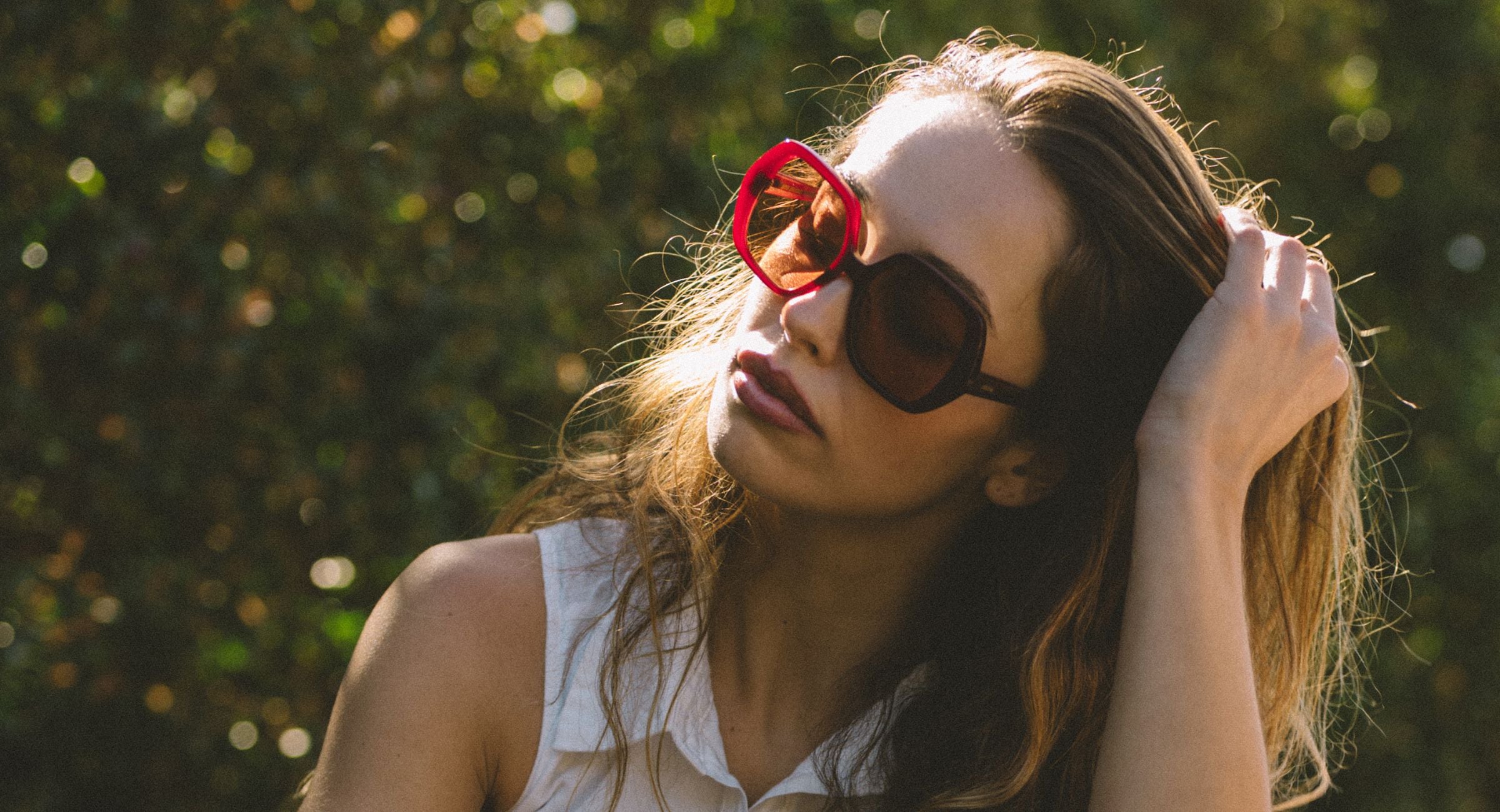 Woman wearing oversized retro red sunglasses with a blurred green background